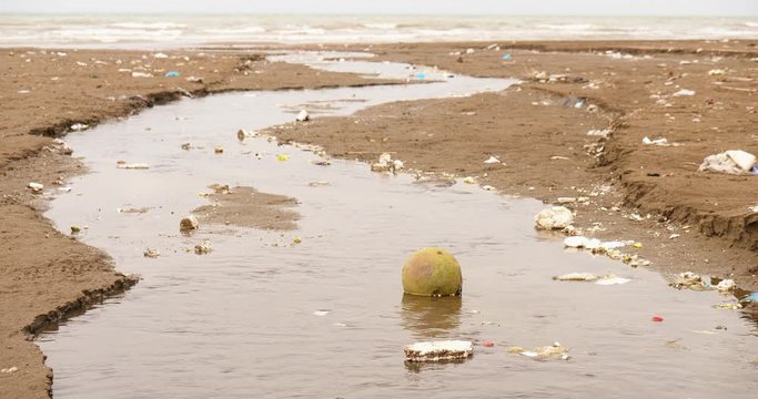 A shot from an small sewage canal flows through the beach to the sea 3 An steady shot of a small canal out of a sewage pipe flows toward the nature and sea with different types of pollution no people