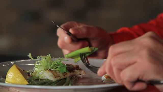 A man eats blanched asparagus and grilled fillet of pike perch, served with lemon and herbs.close-up