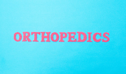 Fototapeta na wymiar Orthopedics inscription in red letters on a blue background. The concept of the section of medicine and treatment of injuries of the joints and spine. Endoprosthetics and arthroscopy.
