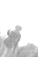Black and white photo of Smiling and healthy senior woman throwing disc in park