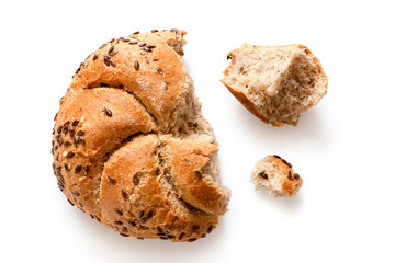 Broken whole wheat kaiser roll with linseeds and sesame seeds isolated on white. Small and big pieces. Top view.