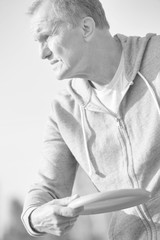 Black and white photo of Healthy senior man throwing disc in park