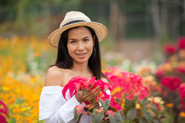 Asian women black long hair in white shirt and hat are enjoying red flowers in the park outdoor garden flower field.