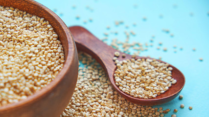 White quinoa seeds on a blue background. quinoa in bowl and a spoon on kitchen table top view. Healthy and diet superfood product.