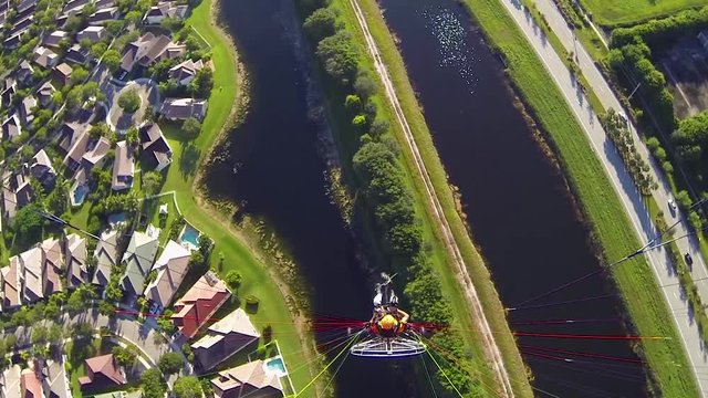 Paramotor pilot flying over a split river along a neighborhood and a highway