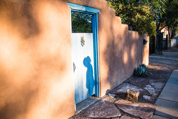 Fototapeta premium The shadow of a young girl on a gated adobe wall.