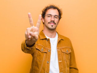 young handsome man smiling and looking friendly, showing number two or second with hand forward,...