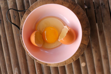 shell with egg and open Eggs in a pink bowl Placed on the butcher on Bamboo battens.Top view closeup.
