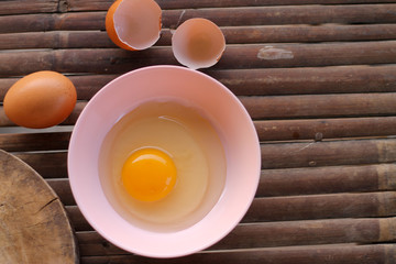 shell with egg and open Eggs in a pink bowl Placed near to the butcher on Bamboo battens.Top view closeup.