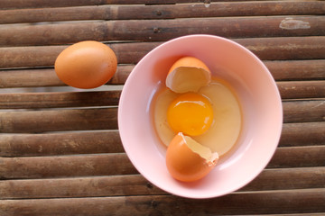 shell with egg and open Eggs in a pink bowl on Bamboo battens. Top view closeup