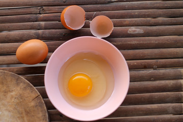 shell with egg and open Eggs in a pink bowl Placed near to the butcher on Bamboo battens.Top view closeup.