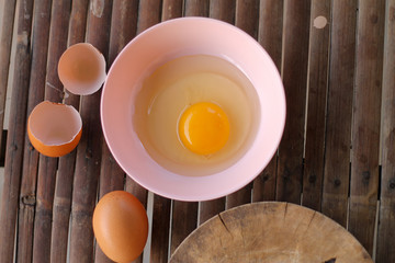shell with egg and open Eggs in a pink bowl Placed near to the butcher on Bamboo battens.Top view closeup.