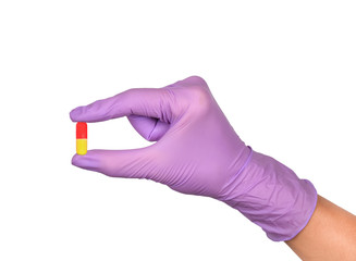 Hand in latex medical glove holding a pill isolated on white.