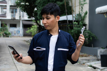 An asian man in mechanic suit is holding wrench and mobile phone