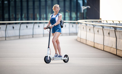 Young woman riding an electric scooter on modern buildings background
