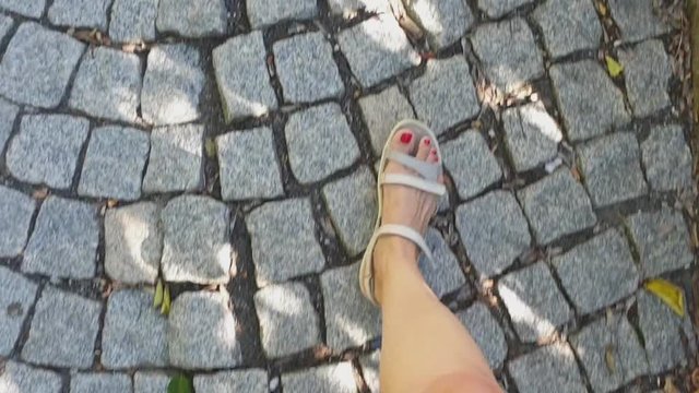 female legs in grey sandals walk along a cobblestone pavemen, first-person view, 4k