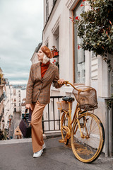 Outdoor full-length autumn portrait of young happy smiling fashionable lady wearing trendy leather beret, turtleneck, beige houndstooth blazer, wide trousers, white sneakers, posing in Parisian street