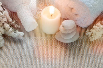 Spa treatments set with herbal compressing ball, oil bottle, candles and towel on bamboo plate background.