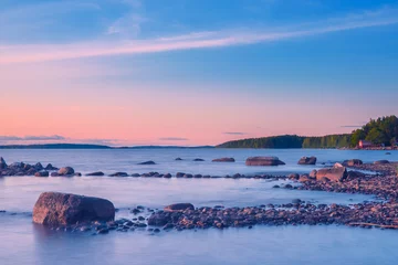 Langzeitbelichtung des Sonnenuntergangs am Paijanne-See. Schöne Landschaft mit Steinstrand, Pinienwald und Wasser. See Paijanne, Finnland. © Della_Liner