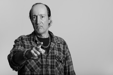 Studio shot of mature gangster man looking angry while pointing finger at camera