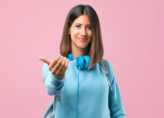 Young student girl with blue sweater and headphones presenting and inviting to come with hand. Happy that you came on pink background