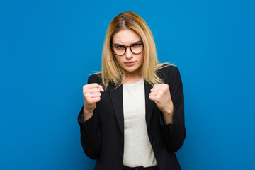 young pretty blonde woman looking confident, angry, strong and aggressive, with fists ready to...