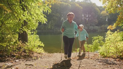 Senior women Nordic walking, enjoying nature in sunny autumn park. Slow-motion shot