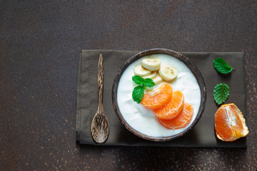 Greek yogurt with orange and a banana mint in a rustic bowl on old kitchen table.  , food and healthy meal concept, top view, copy space.