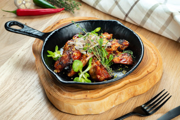 Grilled chicken wings in honey and beer sauce served in a decorative pan with herbs. Close up, selective focus. Wooden background. Food photo