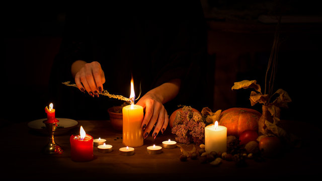 Witch Make A Spell On The Altar In The Dark. Female Hands With Sharp Black Nails Burning Magic Herb Among Candles, Pumpkin, Nuts, Dry Leaves, Selected Focus, Low Key