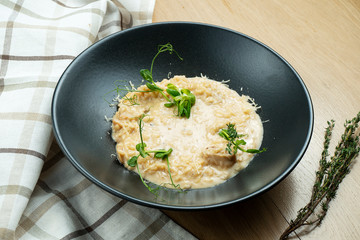 Traditional risotto with porcini mushrooms, cheese and microgreen in stylish black bowl on wooden background. Close up, selective focus. Italian cuisine