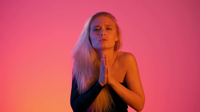 Young beautiful caucasian blonde woman saying please begging praying in neon lights at pink gradient background isolated in studio