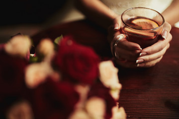 Young bride drinking tea. Wedding bouquet on a wooden table in a restaurant. Cropped image of bride which holding a cup of tea with lamon