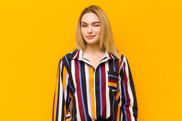 young blonde pretty woman looking happy and friendly, smiling and winking an eye at you with a...