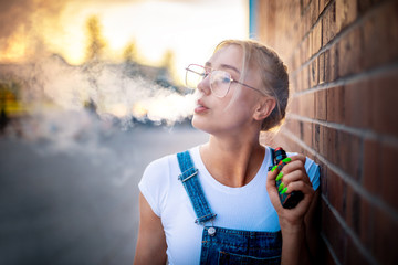 Modern girl outdoor smoking vaping electronic cigarette making big smoke cloud