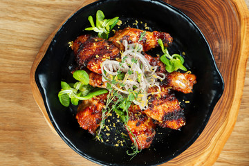 Grilled chicken wings in honey and beer sauce served in a decorative pan with herbs. Close up, selective focus. Wooden background. Food photo