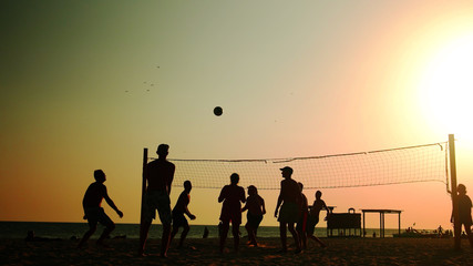 Beach volleyball players at sunset. Group of friends having fun on the beach. Weekend activity concept.