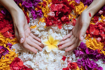 Top view woman's hands holding frangipani on flowers petals in bath tub in luxury bathroom in hotel. Spa, self care, organic and skin care, beauty treatment concept.