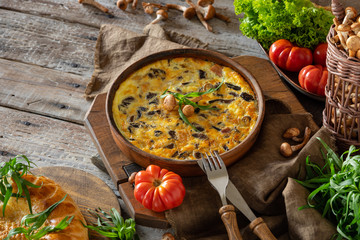fritata or quiche with agaric mushrooms and cheese inceramic baking dish . Garnish with fresh tomatoes, lettuce and tarragon on a wooden table. Traditional Italian menu concept. Horizontal © Елена Григорович