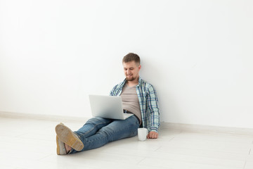 Positive young man in casual clothes and glasses surfing the Internet using Wi-Fi and a laptop in search of rental housing. Housewarming and apartment search concept, copy space