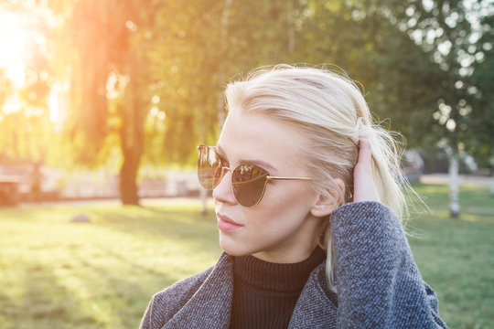 Blonde girl with hipster eyeglasses looking at the camera posing outdoors in the urban park