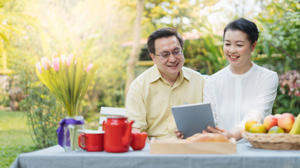 Portrait of happy asian senior couple using digital tablet while relaxing and picnic outdoors.