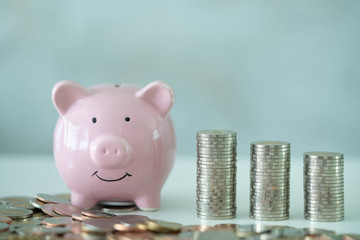 Pink piggy bank on table with stack and pile of coins. Savings concept.
