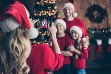 Blurry photo of mom making photo of two children and dad near decorated garland newyear tree indoors family x-mas atmosphere wear santa caps and red sweaters