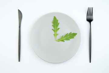 Arugula leaves on a gray plate in the form of hour hands. The concept of proper and dietary nutrition.
