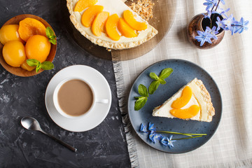 A piece of peach cheesecake on a blue ceramic plate with blue flowers and a cup of coffee on a black concrete background. top view,