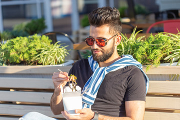 Handsome young arab man are holding wooden sticks chinese noodle. Delicious asian cuisine concept.