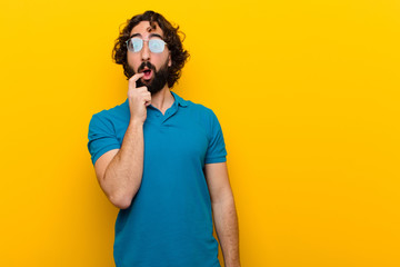 young crazy man with surprised, nervous, worried or frightened look, looking to the side towards copy space against orange wall © kues1