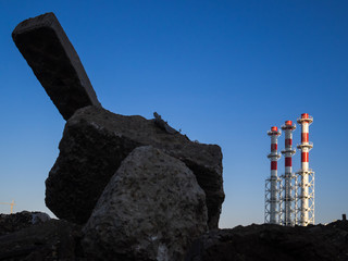 Red-and-white boiler room chimneys against a blue sky. Mountain of stones and debris and pipes boiler station