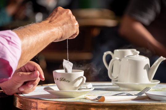 Mans arm dipping tea bag in saucer at a Paris cafe in the morningP